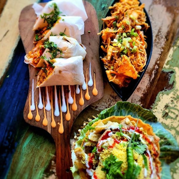 Indian food spread with wraps, noodles, and a chaat dish on a rustic wooden surface.