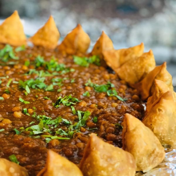 A close-up of Indian chana masala topped with cilantro, surrounded by crispy samosas.