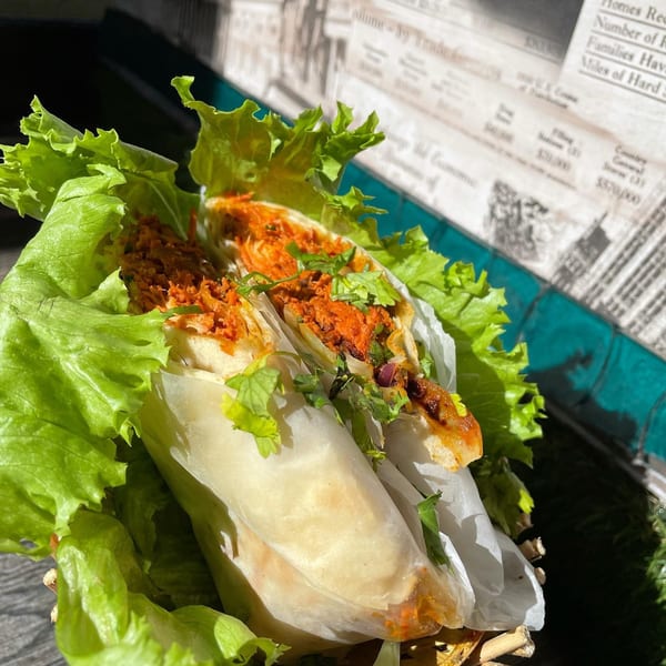 Two Indian wraps with red filling and cilantro, nestled in lettuce leaves, on a newspaper background.